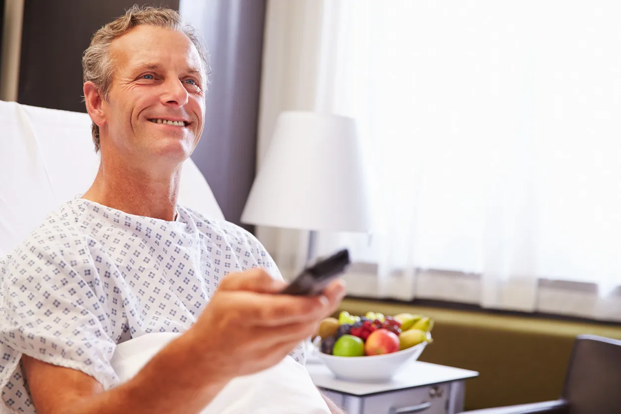 Smiling patient in a hospital bed holding a TV remote control and watching TV