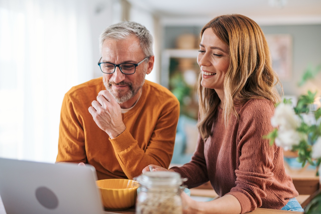 An elderly couple watches a video on a laptop.