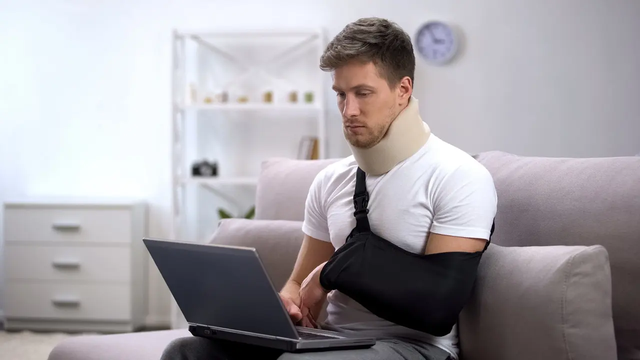 A man with a broken arm and a neck injury is working on his laptop