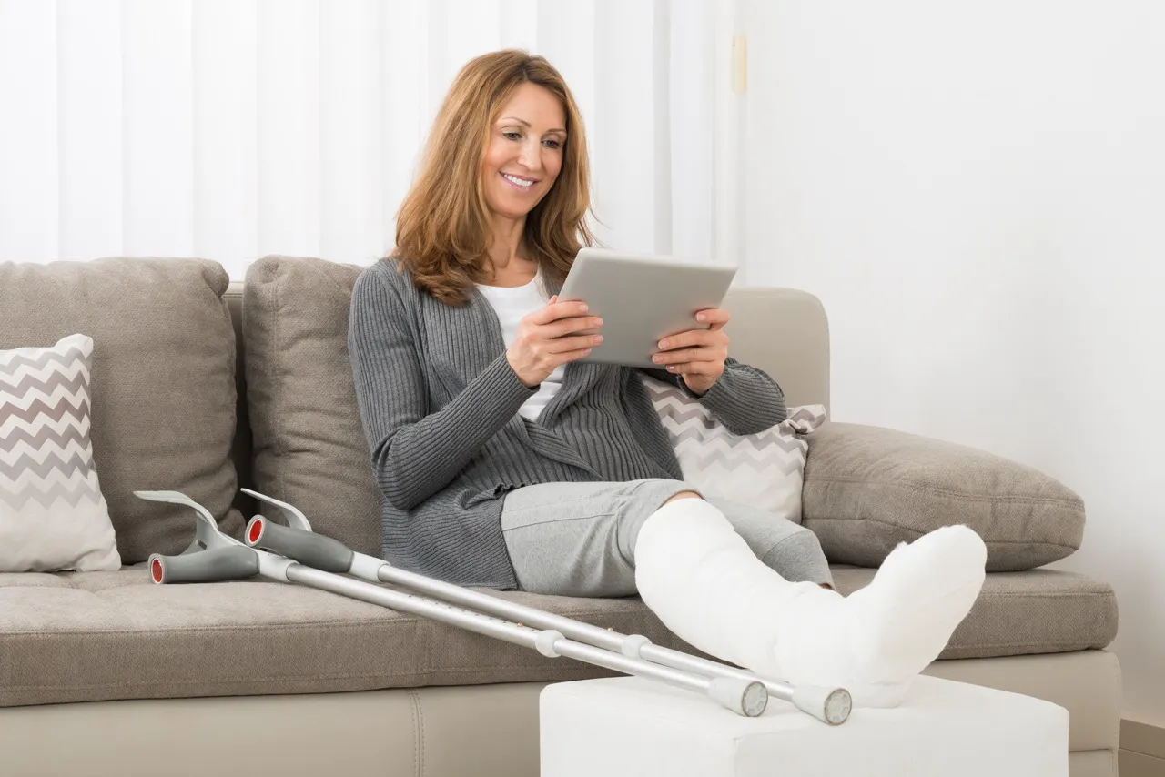 A woman with a broken leg watches on a tablet