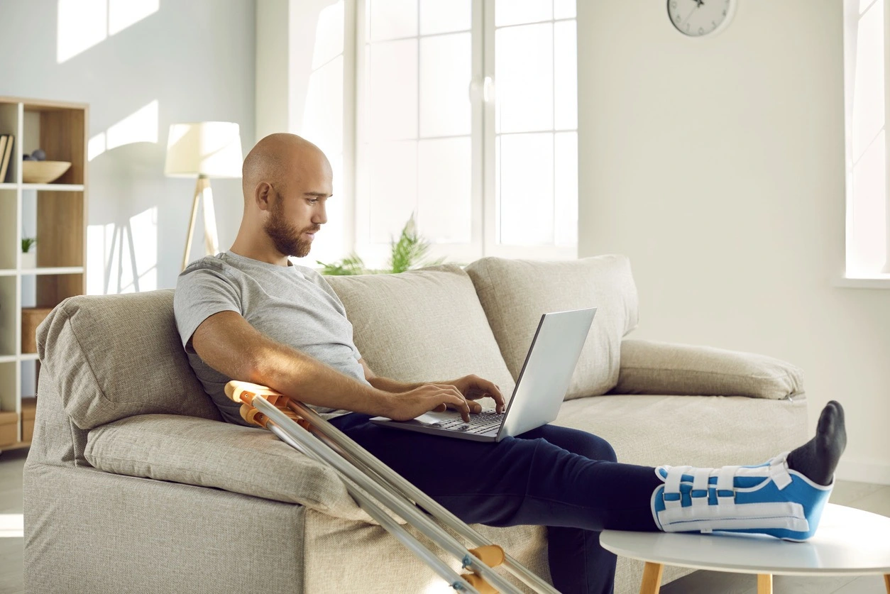 A man with a broken leg is working on his laptop
