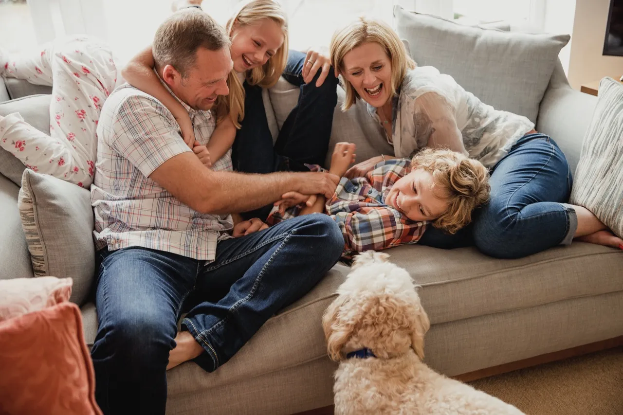 The happy family sits on the sofa and laughs, the dog is beside them